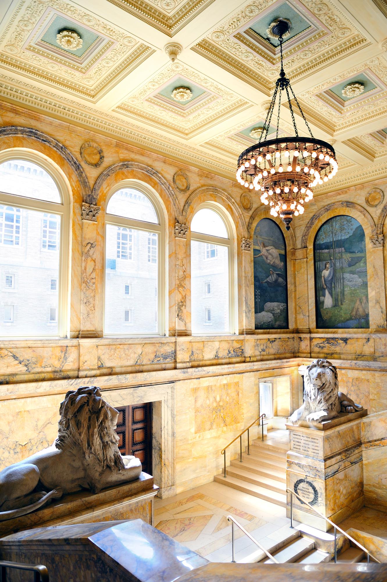 Interior de uma grande biblioteca pública, com arcos de mármore e escadaria